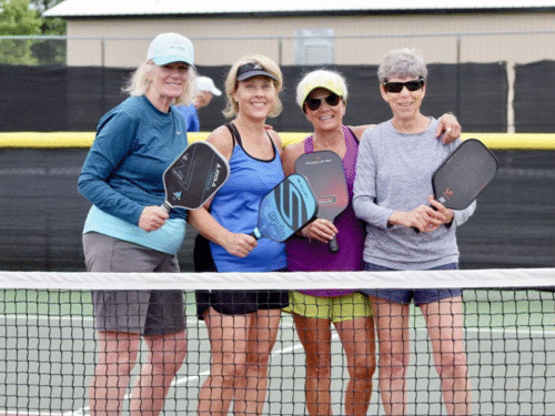 4 women holding pickleball paddles smiling for camera