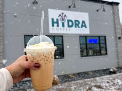Girl holding a coffee in front of Hydra Coffee